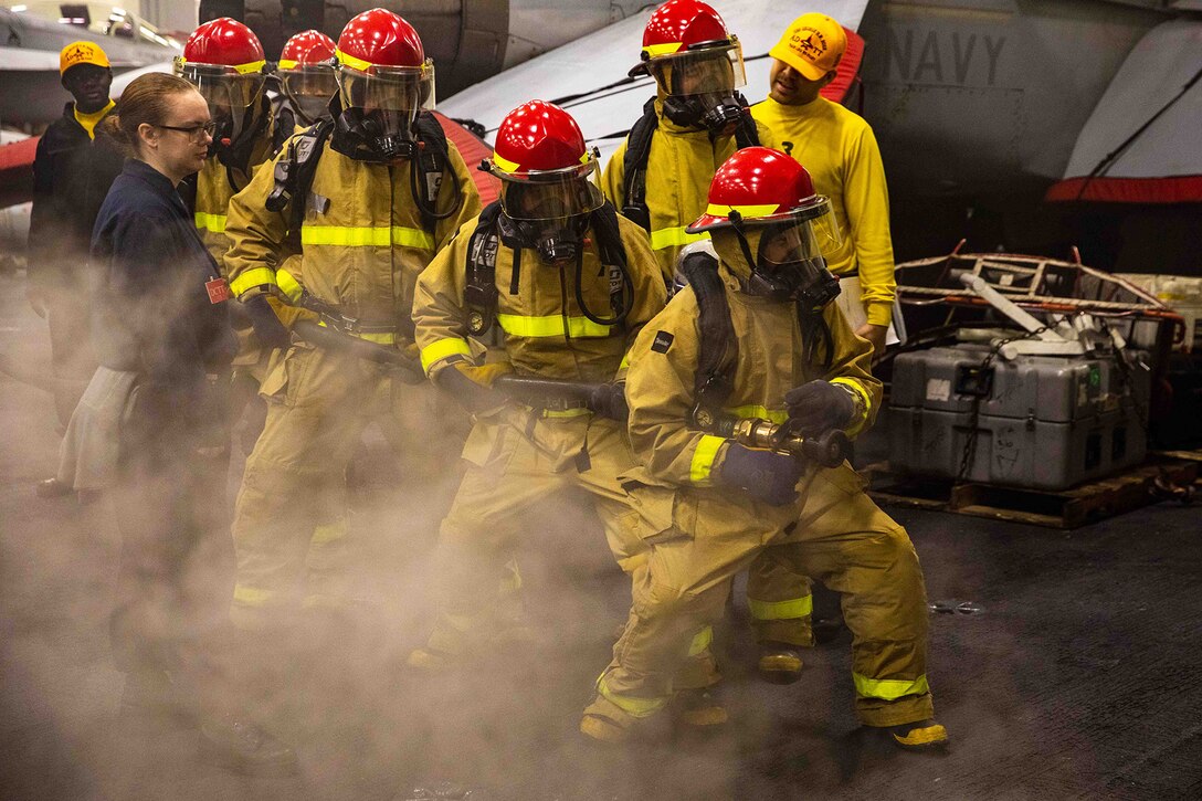 Sailors in firefighting uniforms fight a simulated fire aboard a Navy ship.