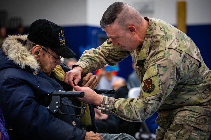 A military officer pins a medal on an older man.