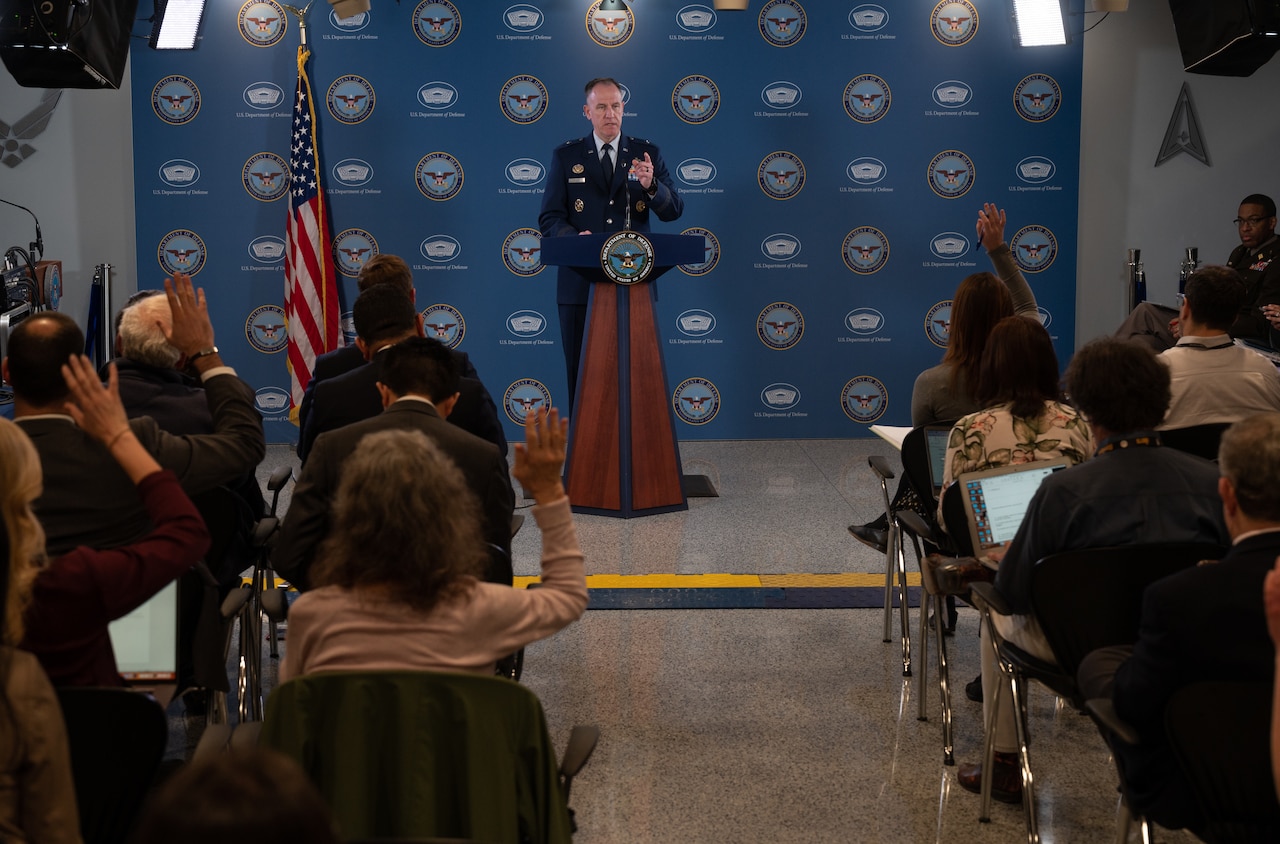 A man speaks from a podium to a reporters sitting in an audience.