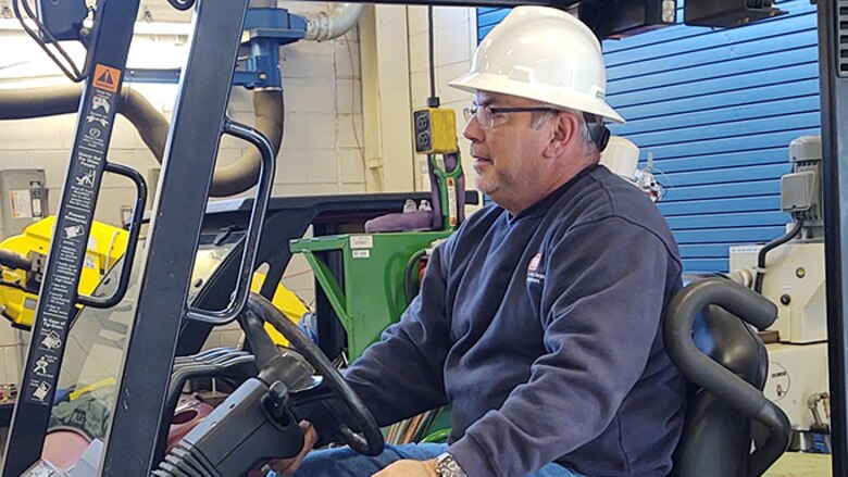 A man with a hard hat operates a forklift.