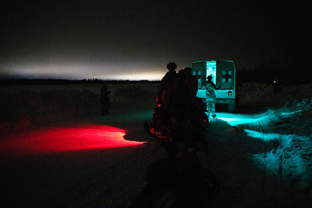 Soldiers stand together with a medical vehicle at night.