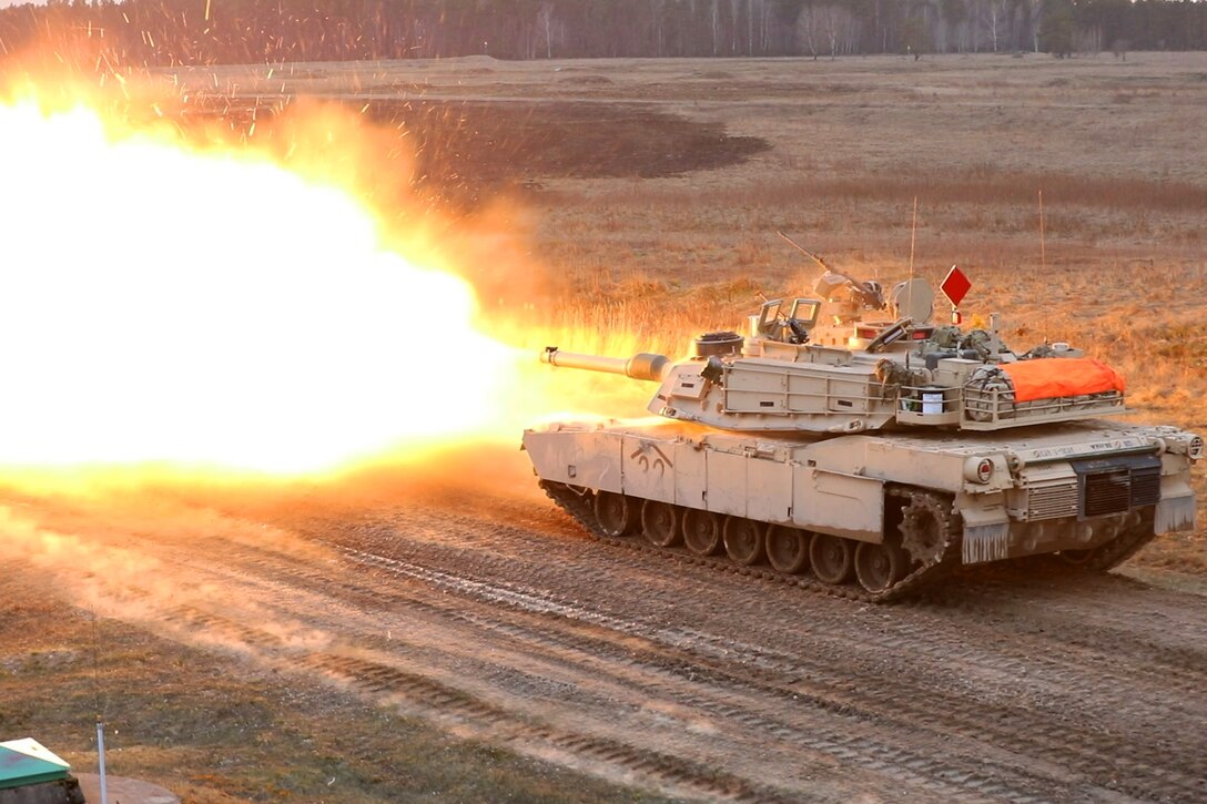 A tank fires its weapon as it moves down a road.