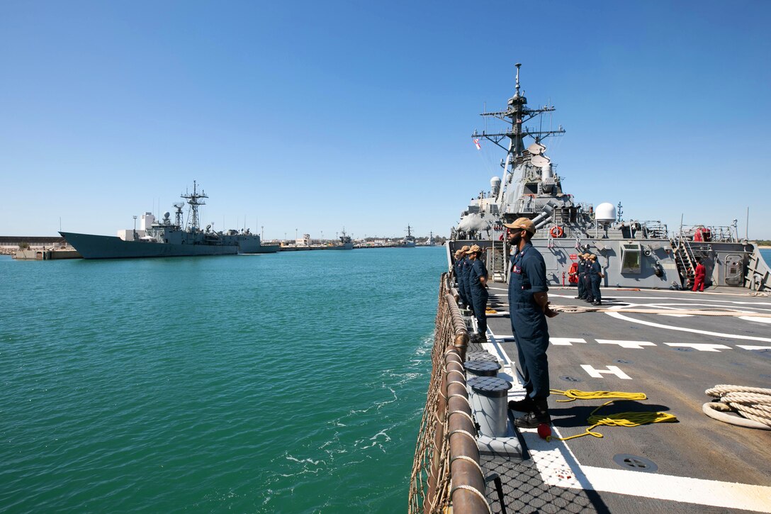 Sailors stand side by side on the edge of a ship.