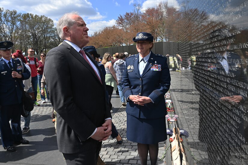 A man and a woman in uniform stand next to the Vietnam Veterans War Memorial.
