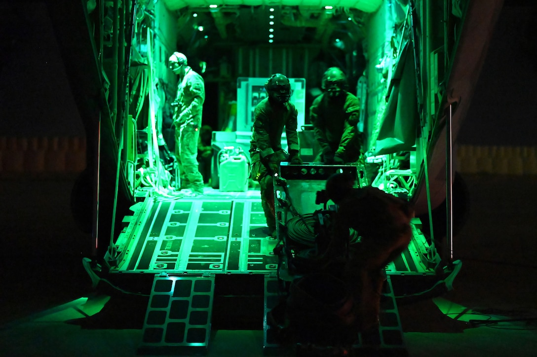 Airmen load equipment into a military aircraft at night.