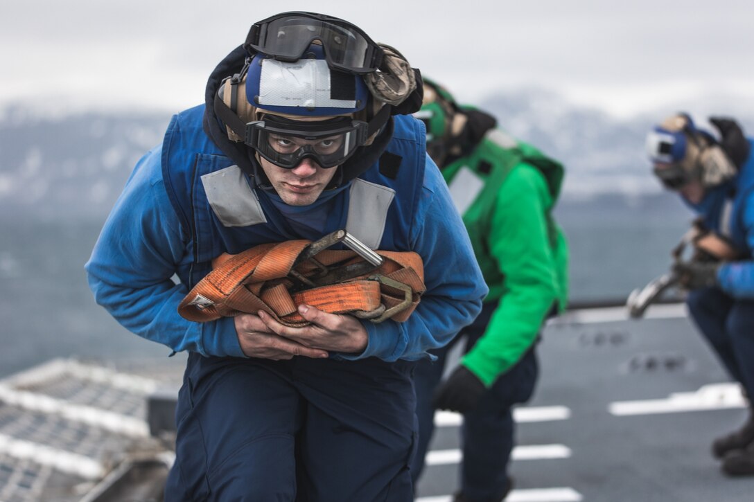 Coast Guard members lean forward and move away from a helicopter.