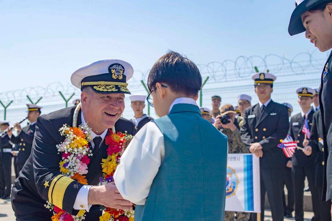 A sailor gives a child a gift as others watch.