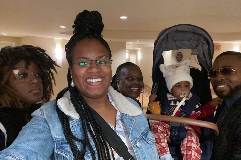 Four civilian adults stand for a photo with a baby.