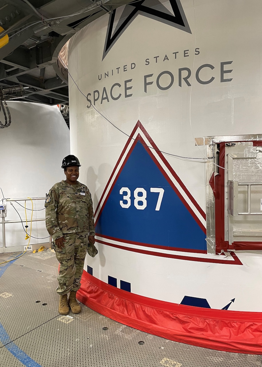 A guardian wearing a hardhat stands by a curved wall with Space Force signage.