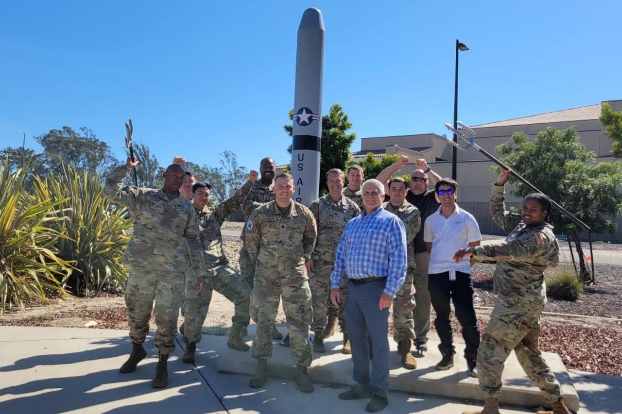 Service members and civilians pose for a photo in front of an Air Force static display outdoors.