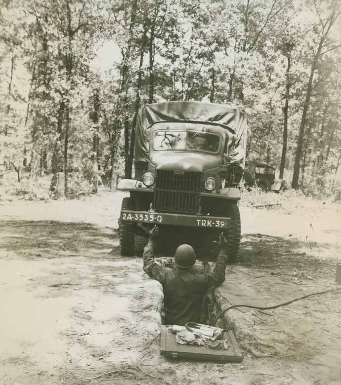 A man standing in a chest-high pit directs a vehicle to drive above him.