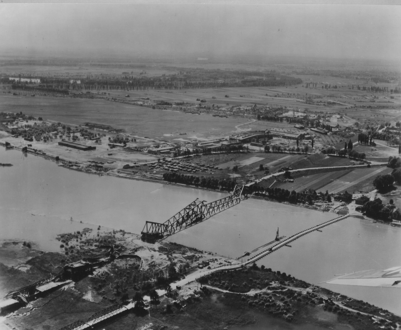 An aerial view shows a river with two bridges; one appears to be damaged.
