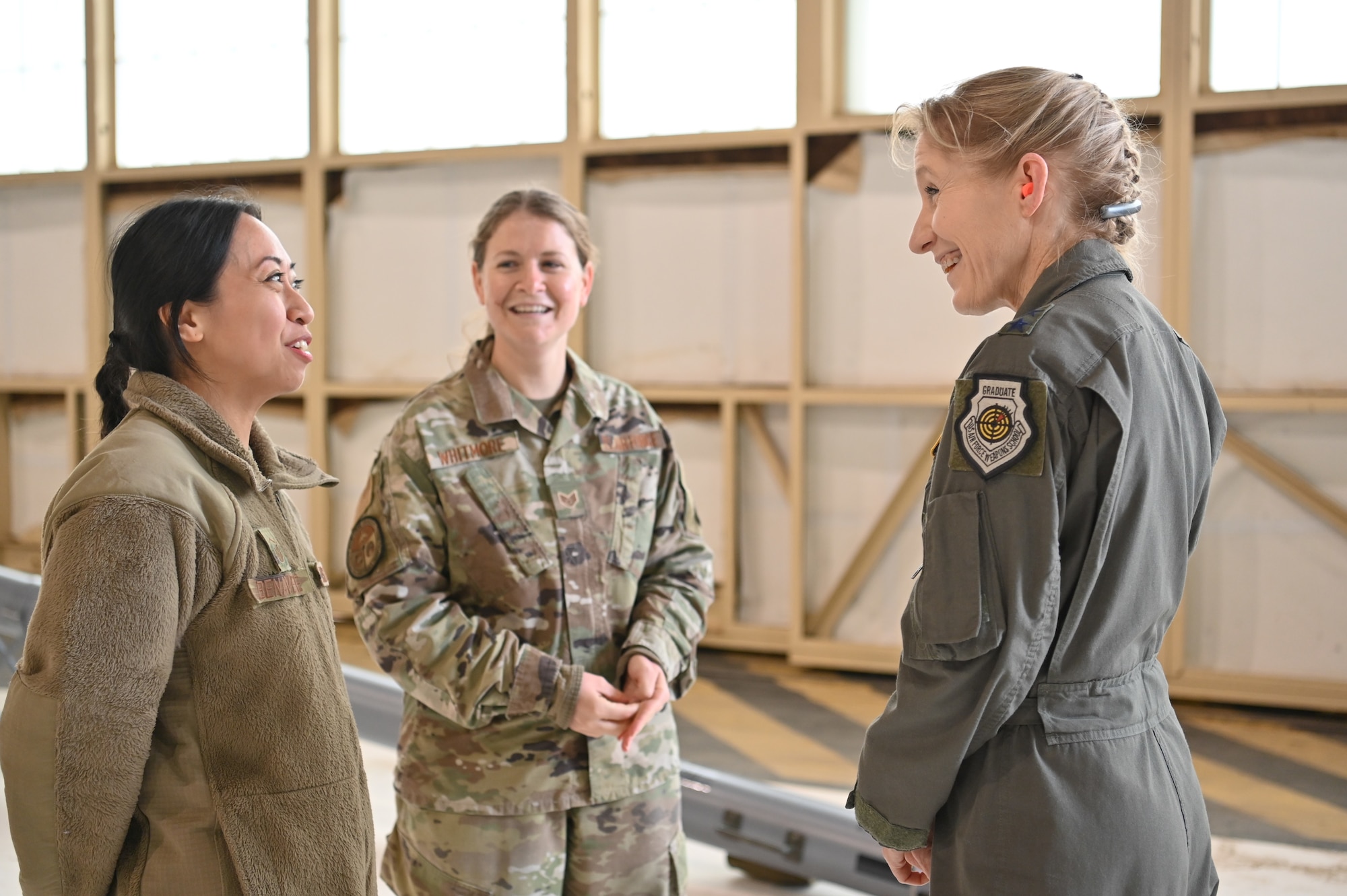 Three female Airmen talking inside hangar
