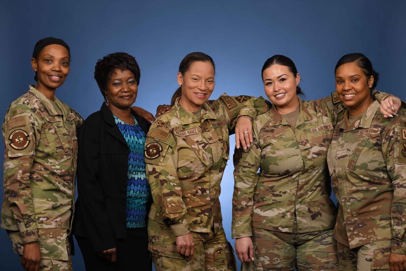 Four women of color in uniform stand together in uniform alongside one in civilian clothes.