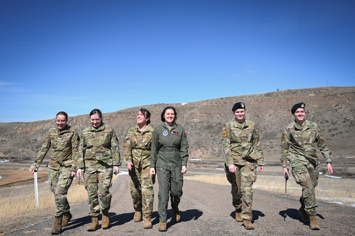 A group of six women in military uniform walk side-by-side together on an asphalt road.