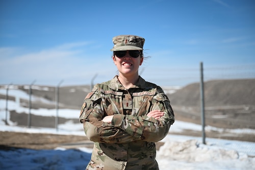 A woman in military uniform and black sunglasses stands in the middle of frame.