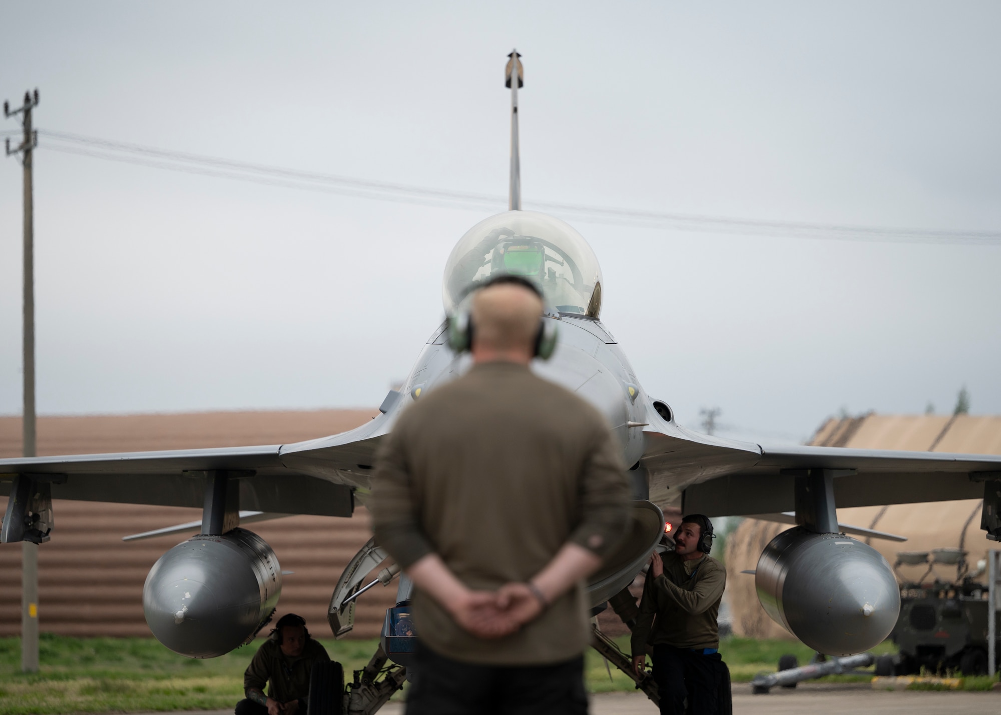 A maintainer stands in the foreground while an aircraft in front of him is in focus