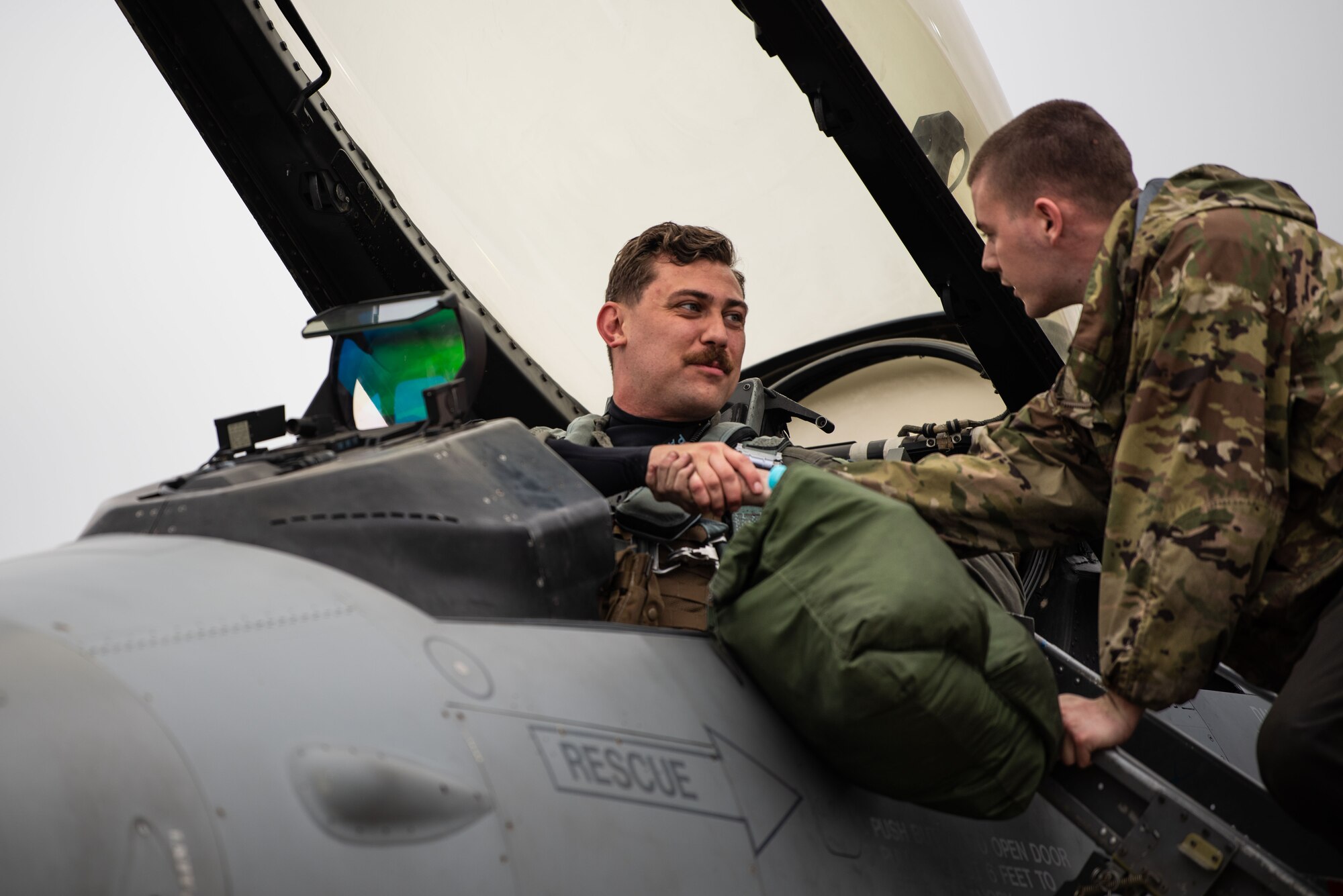 A pilot and a maintainer smile while shaking hands before taxiing for takeoff