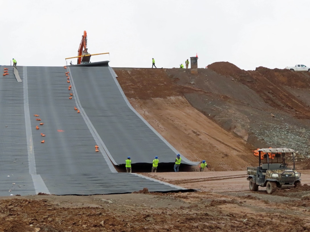 Contractors role out a liner material across the slope/embankment of the dam.