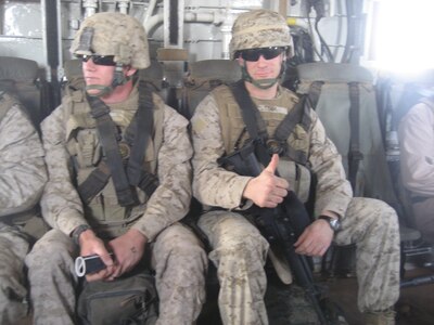 Two men in military uniforms sitting on the inside of military aircraft