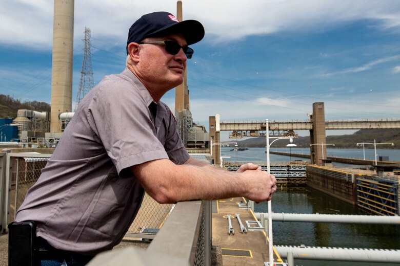 A man stands on a platform overlooking a river.