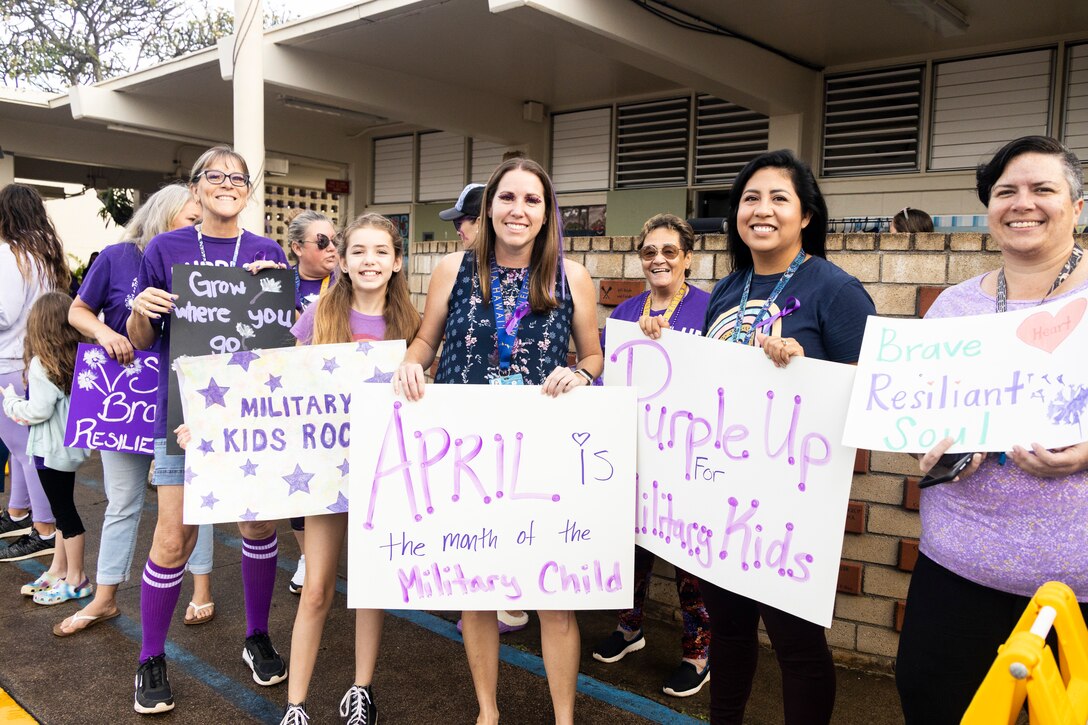 Mokapu Elementary teachers and staff hold up a sign welcoming students during Purple Up Day at Mokapu Elementary School, Marine Corps Base Hawaii, April 19, 2023. Mokapu Elementary invited students and staff to wear purple, make signs, and greet others at the entrance in order to celebrate Month of the Military Child. (U.S. Marine Corps photo by Cpl. Samantha Sanchez)
