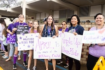 Mokapu Elementary teachers and staff hold up a sign welcoming students during Purple Up Day at Mokapu Elementary School, Marine Corps Base Hawaii, April 19, 2023. Mokapu Elementary invited students and staff to wear purple, make signs, and greet others at the entrance in order to celebrate Month of the Military Child. (U.S. Marine Corps photo by Cpl. Samantha Sanchez)