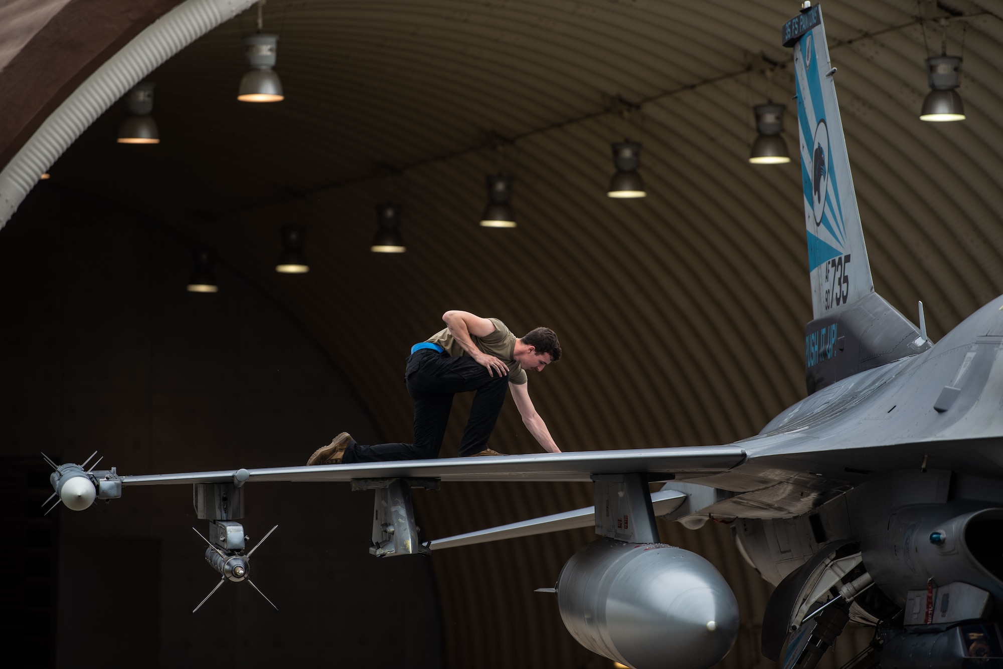 An aircraft maintainer kneels on the wing of an aircraft