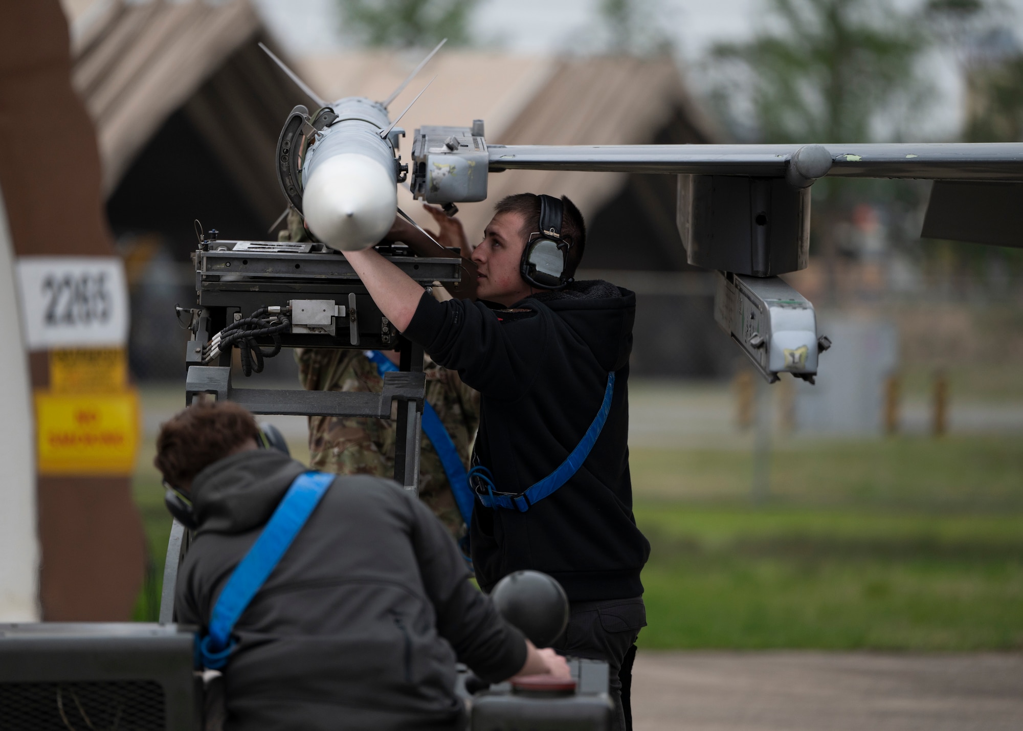A side profile of two maintainers loading a munition onto a jet wing