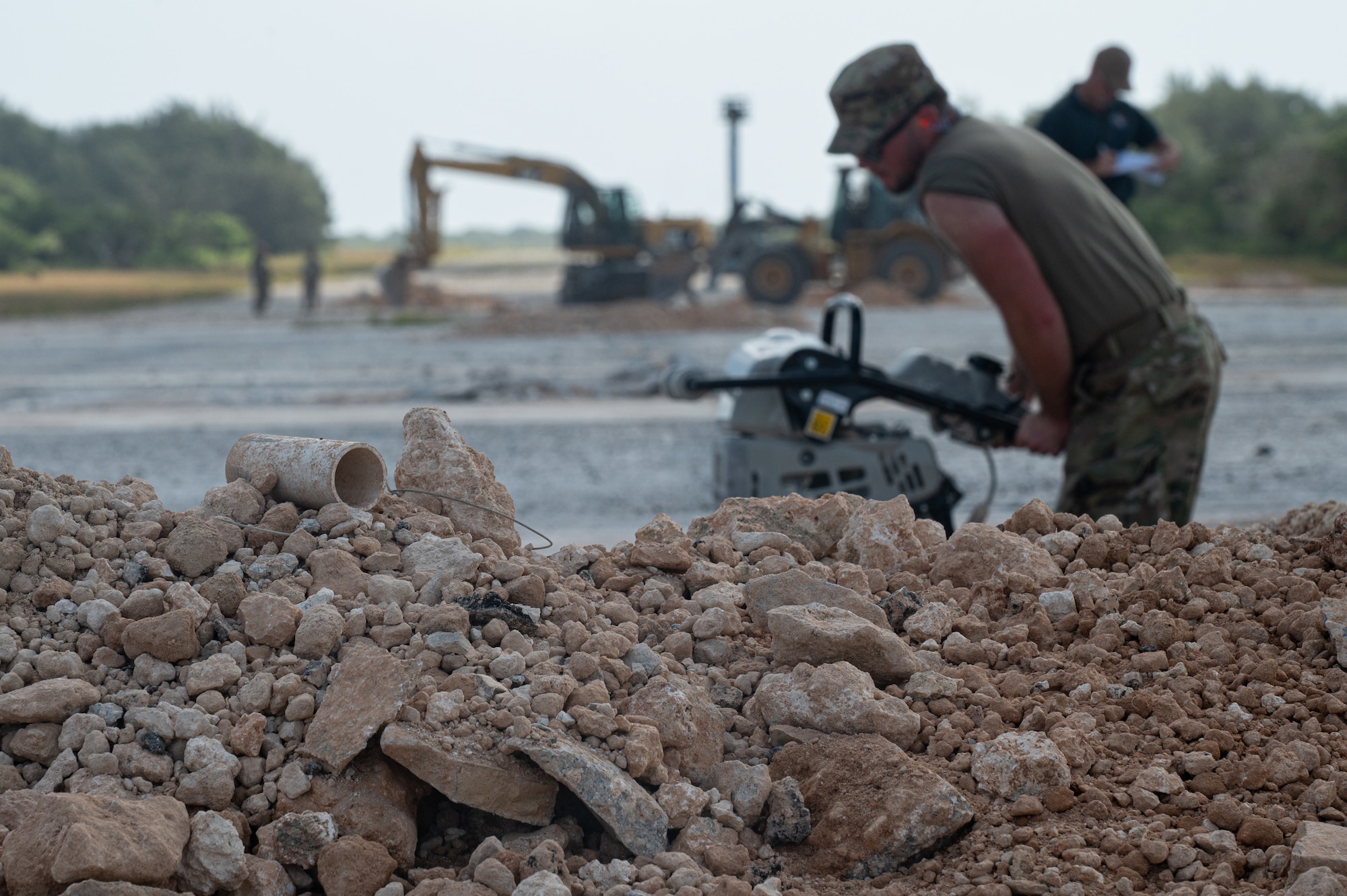 U.S. Air Force Airman 1st Class Cole Masloskie, 36th Civil Engineer Squadron electrical systems technician, uses a tamper to compact dirt and rock during an expedient and expeditionary airfield damage repair demonstration hosted by Headquarters Pacific Air Forces Civil Engineer Division at the Pacific Regional Training Center-Andersen, Guam, April 20, 2023. Sixteen Airmen from the 36th CES were provided two days of vehicle and material familiarization from the 554th Rapid Engineer Deployable Heavy Operational Repair Squadron Engineers and the Air Force Civil Engineer Center to complete airfield damage repair using the smaller packages of Airmen and equipment, called E-ADR. They used their familiarization to validate the E-ADR concept, in support of a Pacific Air Forces agile combat employment, repairing 10 craters with a lighter and leaner vehicle and equipment kit that weighs a fraction of a standard Rapid Airfield Damage Recovery package. (U.S. Air Force photo by Staff Sgt. Suzie Plotnikov)