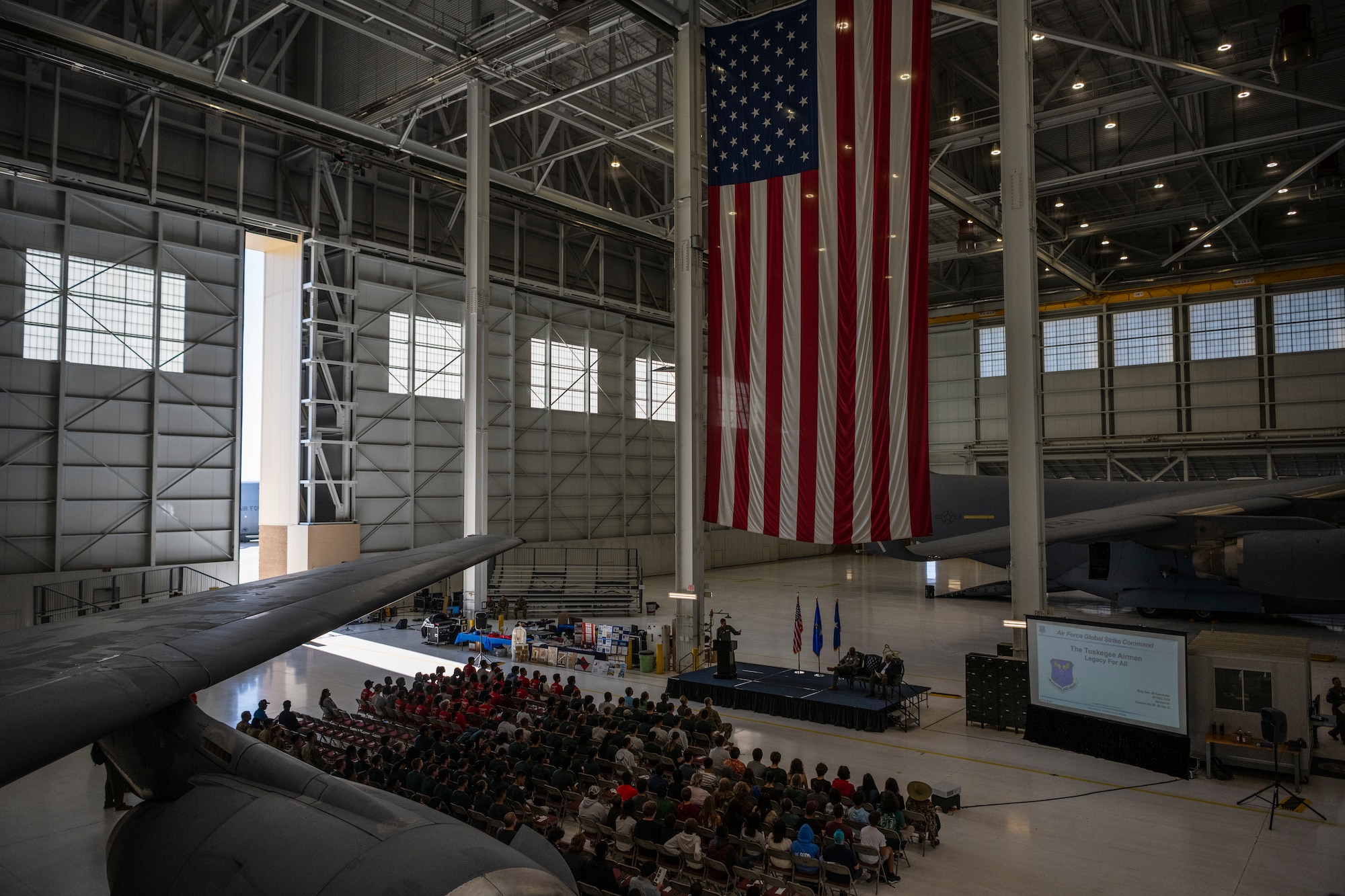 A lot of students sit in chairs listening to a man talk in to a microphone.