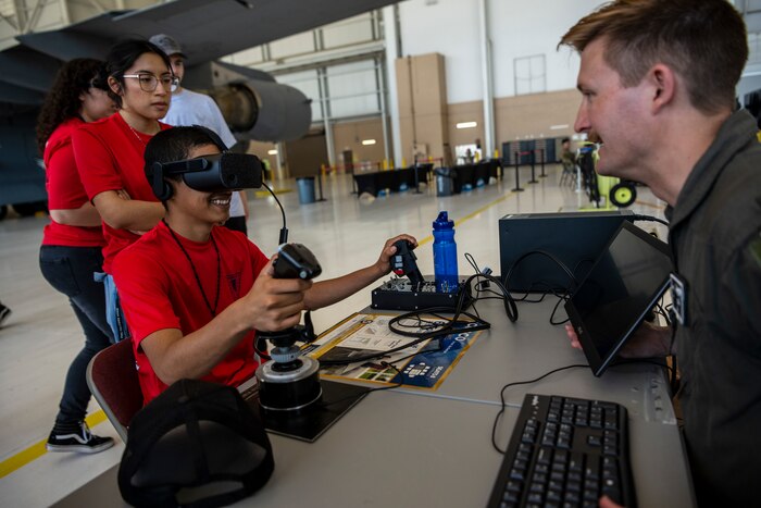 A student wears a VR headset while a man helps him.