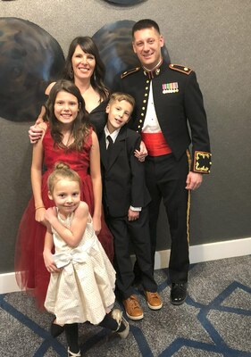 Man in uniform poses for a family photo with his wife, two daughters, and son