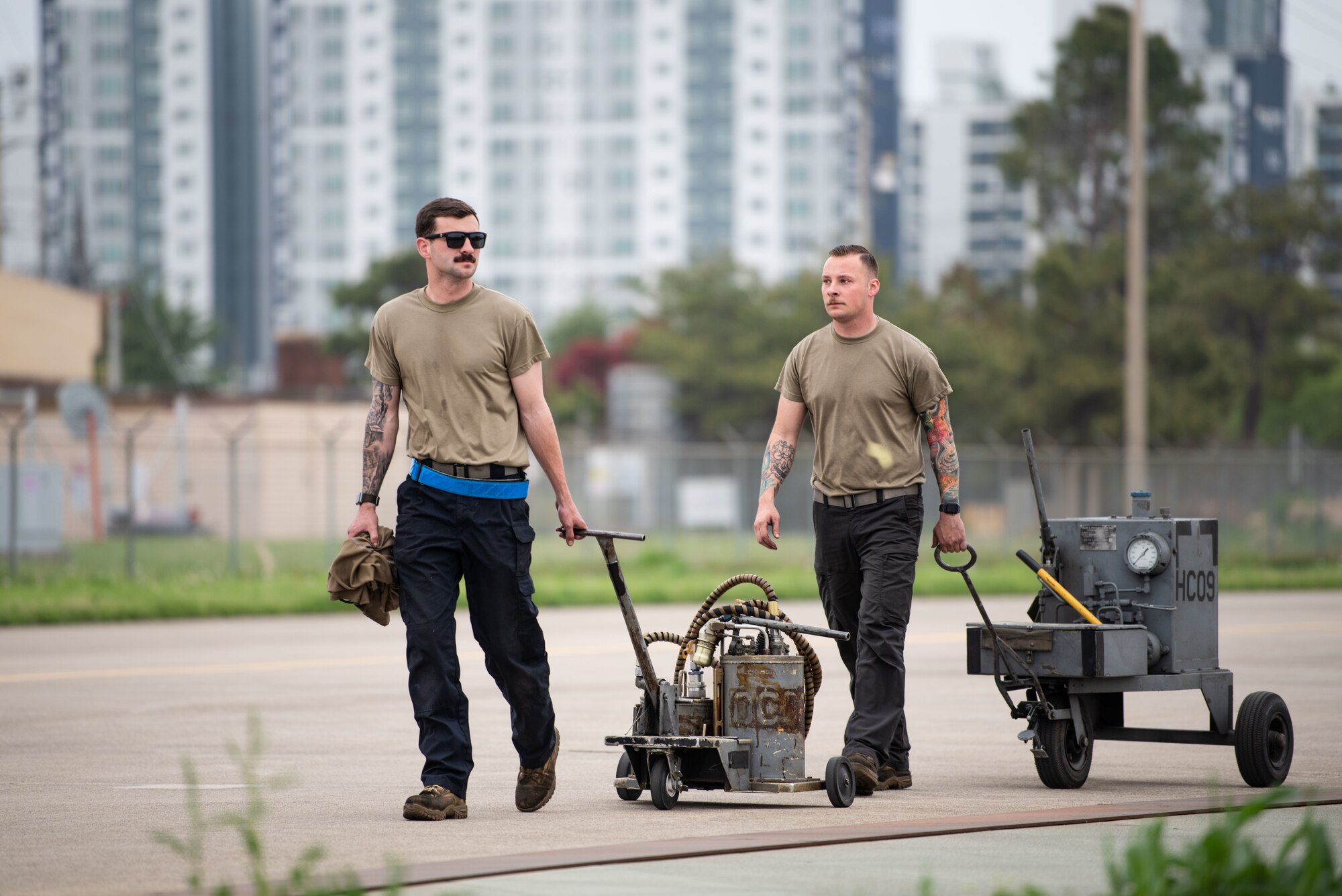 Two maintainers in t-shirts wheel aircraft maintenance equipment to a jet