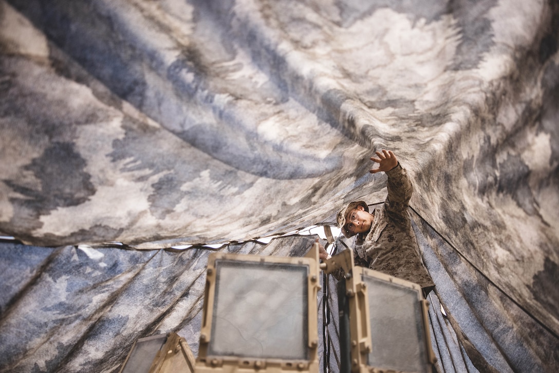 A Marine adjusts an overhead camouflage net.