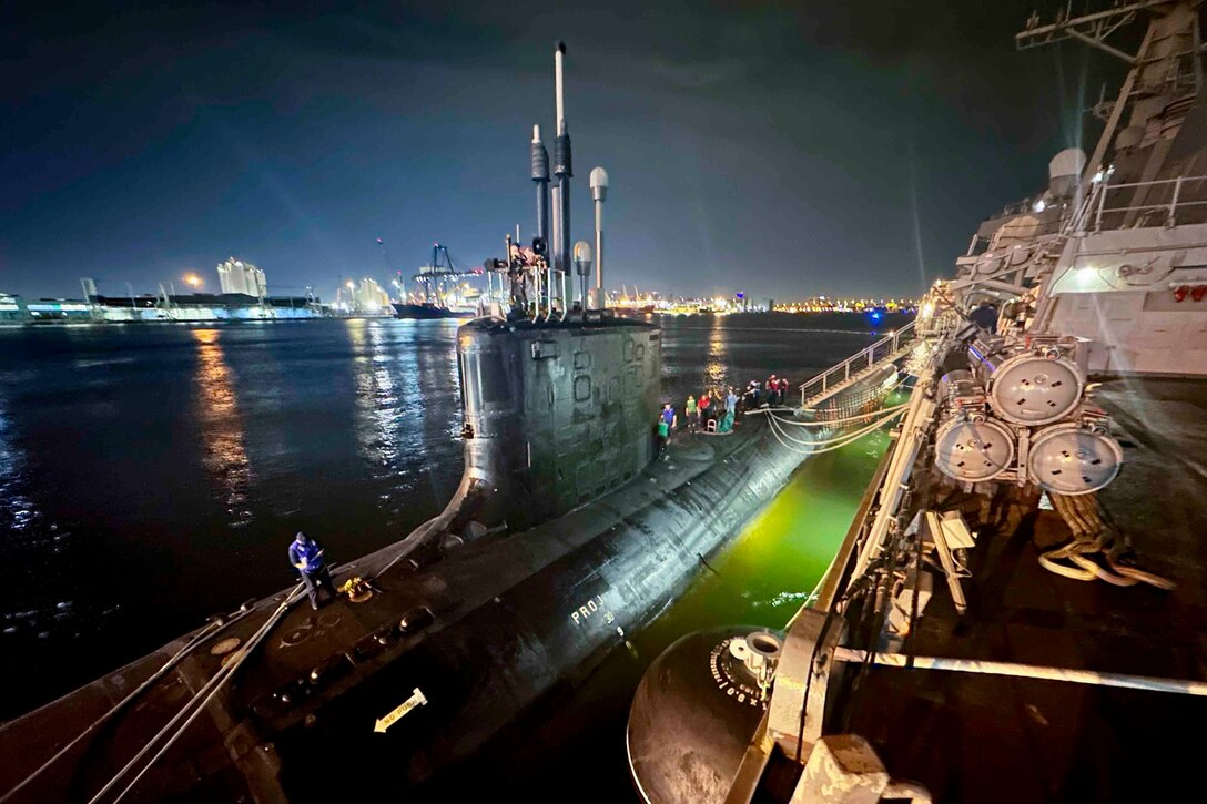 A submarine is moored next to a ship at night.