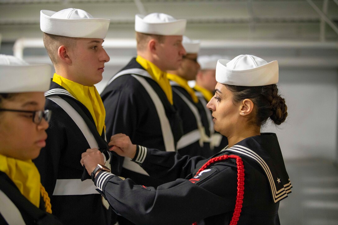 A sailor adjusts the neckerchief of a recruit standing in formation with fellow recruits.