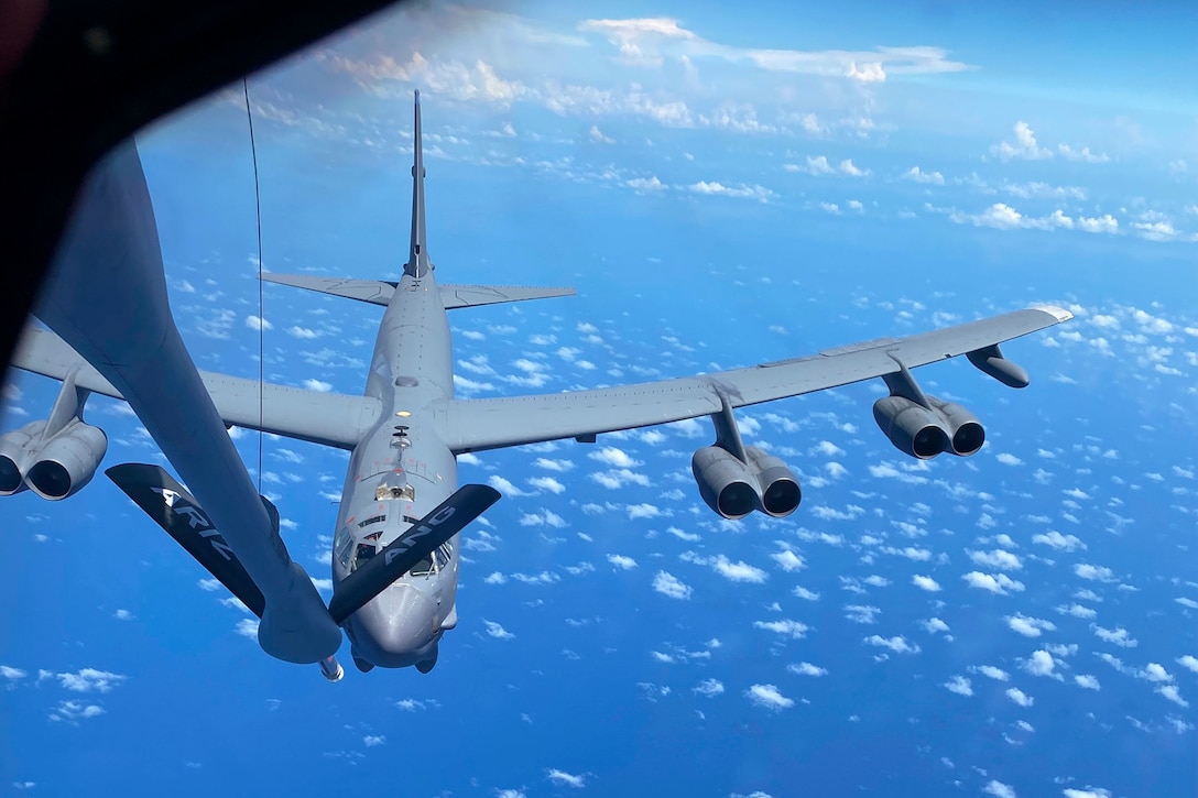 An aircraft receives fuel from an aircraft flying in front of it surrounded by clouds.