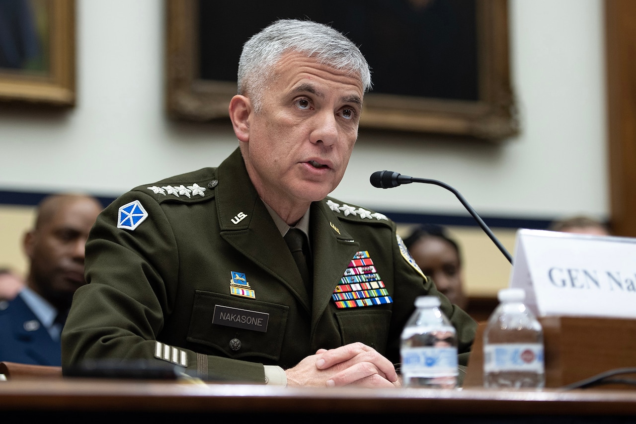 A man in military uniform sits behind a microphone.