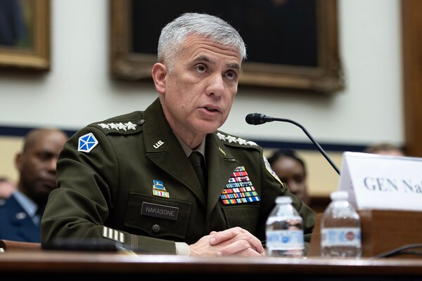 A man in military uniform sits behind a microphone.