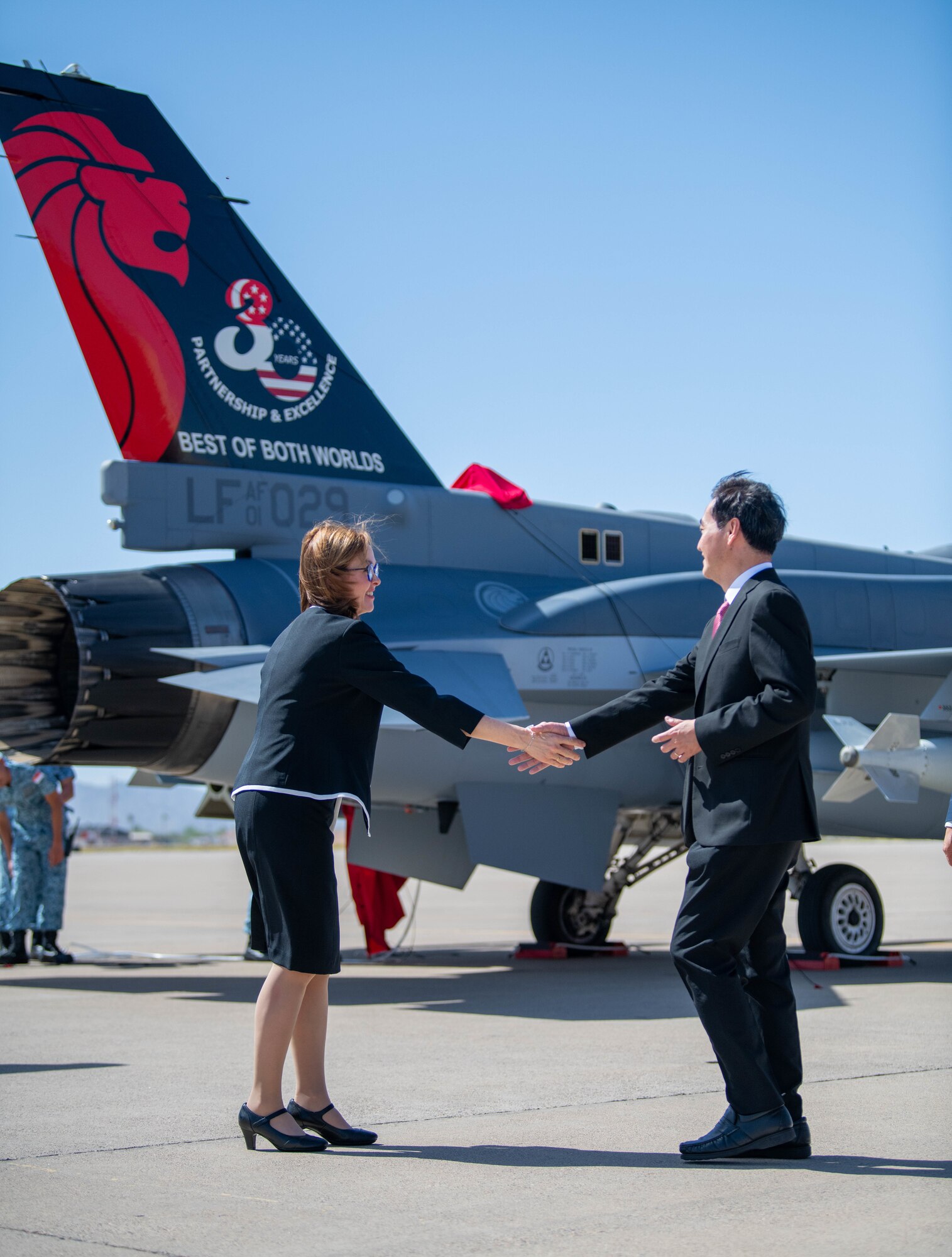 Kelli Seybolt (left), U.S. Air Force International Affairs Deputy Under Secretary, and Heng Chee How (right), Republic of Singapore Senior Minister of State, shake hands in front of a Republic of Singapore Air Force F-16 Fighting Falcon heritage jet during the RSAF Peace Carvin II 30th Anniversary celebration event, April 25, 2023, at Luke Air Force Base, Arizona.