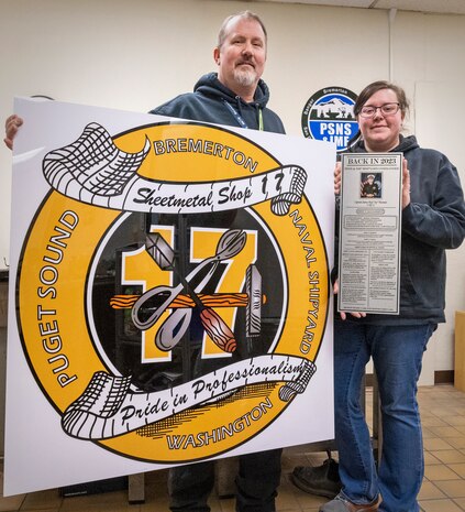 Brett Burton, supervisor, Shop 17, Sheet Metal, and sheet metal mechanic Jazmyn Smith hold the shop's new sign that now hangs outside Building 857 at Puget Sound Naval Shipyard & Intermediate Maintenance Facility in Bremerton, Washington. (U.S. Navy photo by Wendy Hallmark)