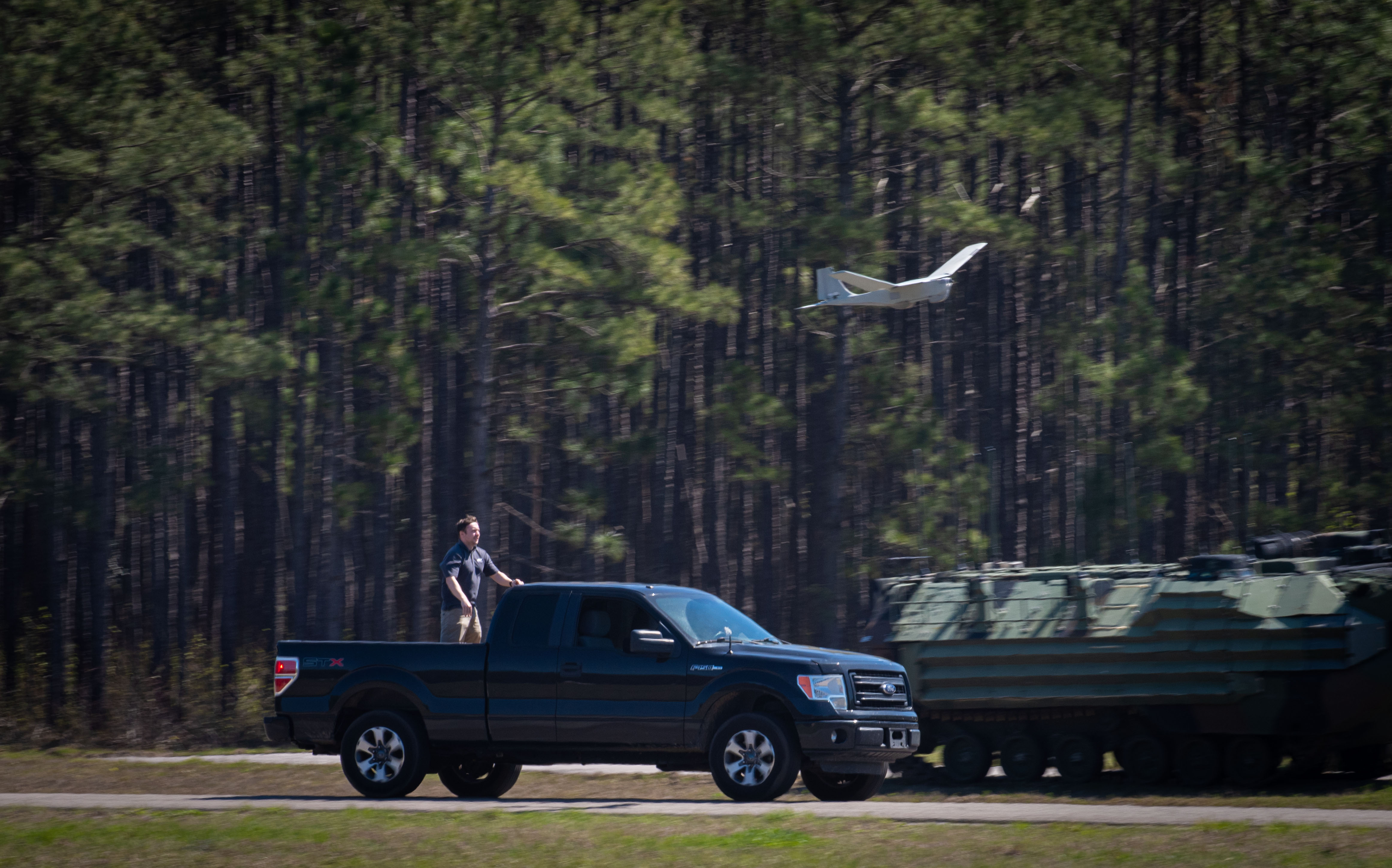 Engineer in the bed of a black truck driving under an unmanned ariel vehicle (UAV)
