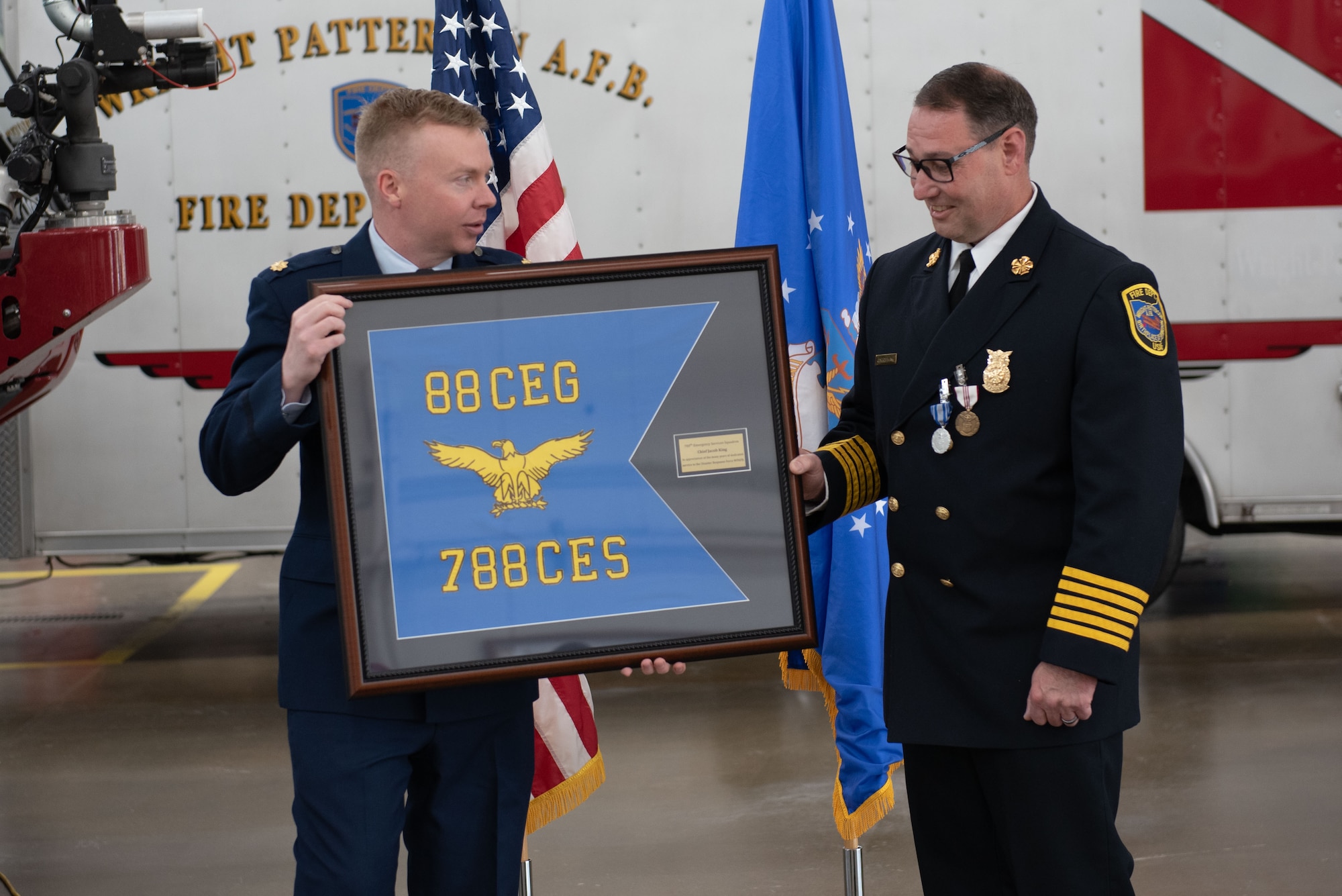 Maj. Nathan Thomsen, left, 788th Civil Engineer Squadron commander, presents Jacob King, WPAFB fire chief, with a squadron gift April 28, 2023, at Wright-Patterson Air Force Base, Ohio. The WPAFB Fire Department celebrated as King retired after a 27-year civil service career. (U.S. Air Force photo by Darrius Parker)
