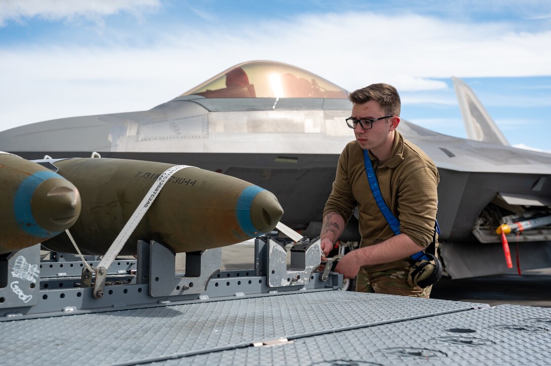 A photo of an Airman stapping bombs to a trailer