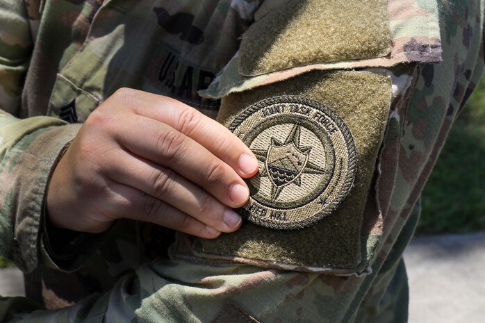A U.S. Army Soldier assigned Joint Task Force-Red Hill (JTF-RH) attaches a unit patch to her uniform at a patching ceremony at task force headquarters on Ford Island, Hawaii, April 28, 2023.