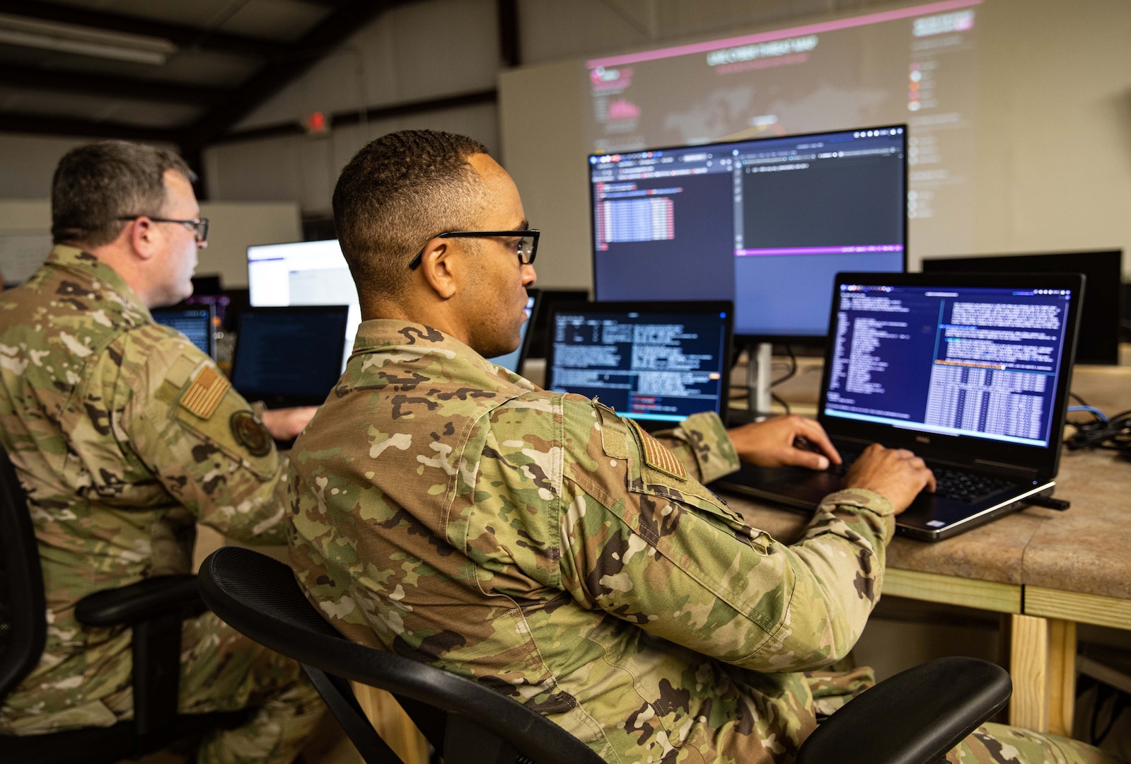 Two service members look at computer screens.