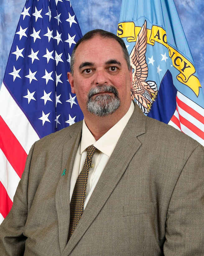 Official photo of Richard TeBeau in brown suit with American and DLA flags in the background