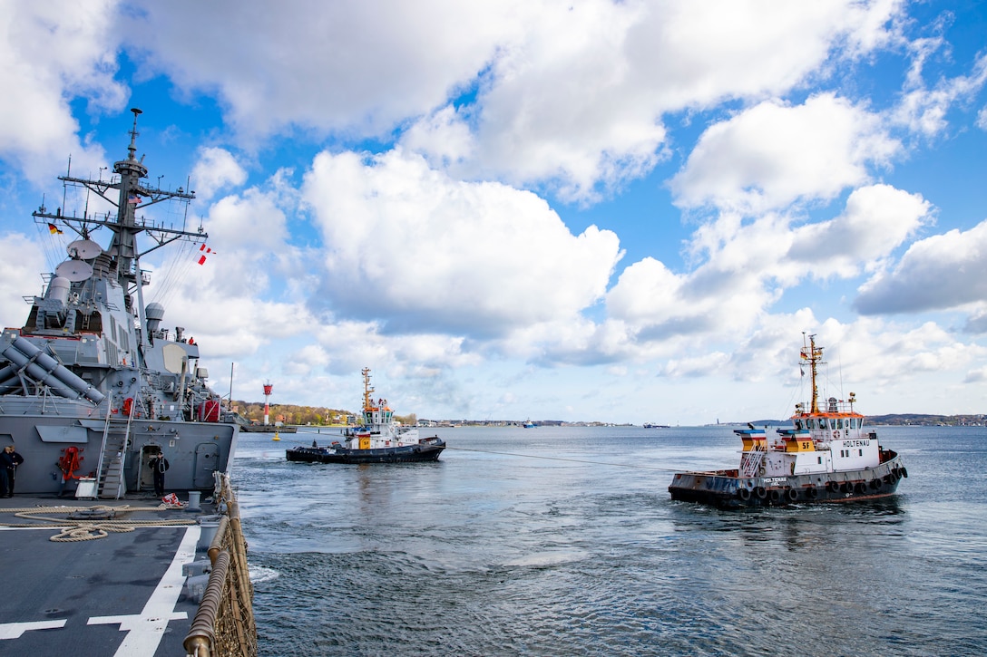 Tug boats maneuver the USS Porter as it departs a port.