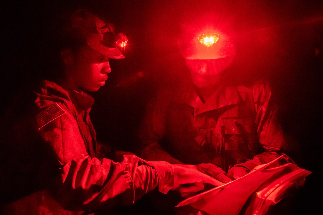 Two service members look at a map at night, illuminated by red headlamps.